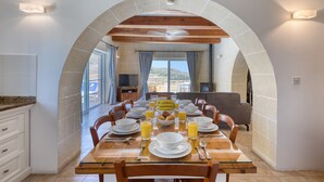 A dining area with a table set for breakfast, a stone archway, and a view of the outdoors. - Rebekah – Ghasri Holiday Home (L-Għasri)