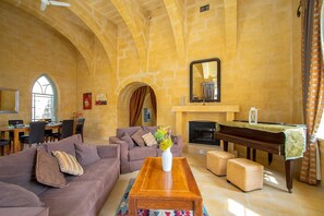 A spacious living room with a fireplace, a dining area, and a large arched window.