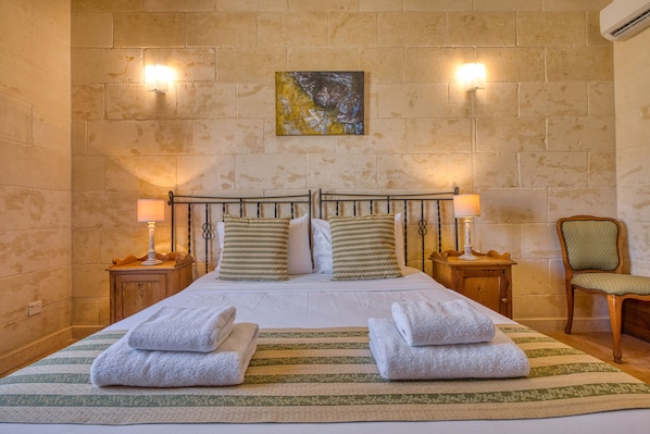 A neatly made bed with pillows, two bedside lamps, a chair, and a painting on the wall.