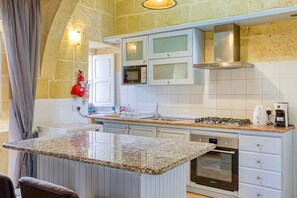 Une cuisine dotée de plans de travail en granit, de meubles blancs, d’un four encastré et d’une hotte de cuisson en acier inoxydable.