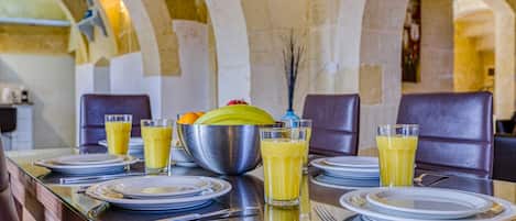 A breakfast table set with plates, glasses, and a bowl of fruit.