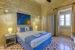 A bedroom with a bed, nightstands, a wardrobe, a window with curtains, and a colorful wall art piece.