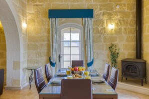 A dining area with a stone wall, a wooden table set for four, and a wood-burning stove. - Girardu - Victoria Holiday Home (Victoria)