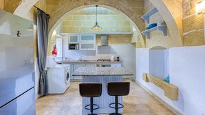 A kitchen with an arched stone ceiling, a central island with stools, and a washing machine. - Girardu - Victoria Holiday Home (Victoria)