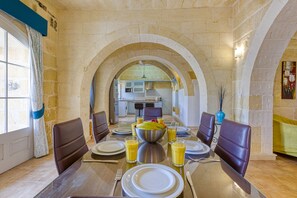 A dining area with a stone archway, a wooden table set for six, and a view into the kitchen.