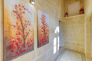 Un couloir aux murs de pierre, orné de deux tableaux représentant des fleurs rouges.