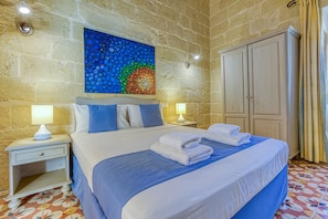 A hotel room with a stone wall, a bed with blue bedding, two bedside tables with lamps, and a large wardrobe. - Girardu - Victoria Holiday Home (Victoria)
