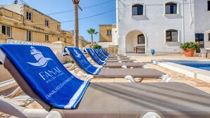 A poolside area with lounge chairs and a building with arched windows. - Hgieri - Ghasri Holiday Home (L-Għasri)