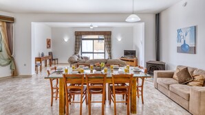 A spacious living area with a dining table set for four, a sofa, a TV, and a fireplace. - Hgieri - Ghasri Holiday Home (L-Għasri)