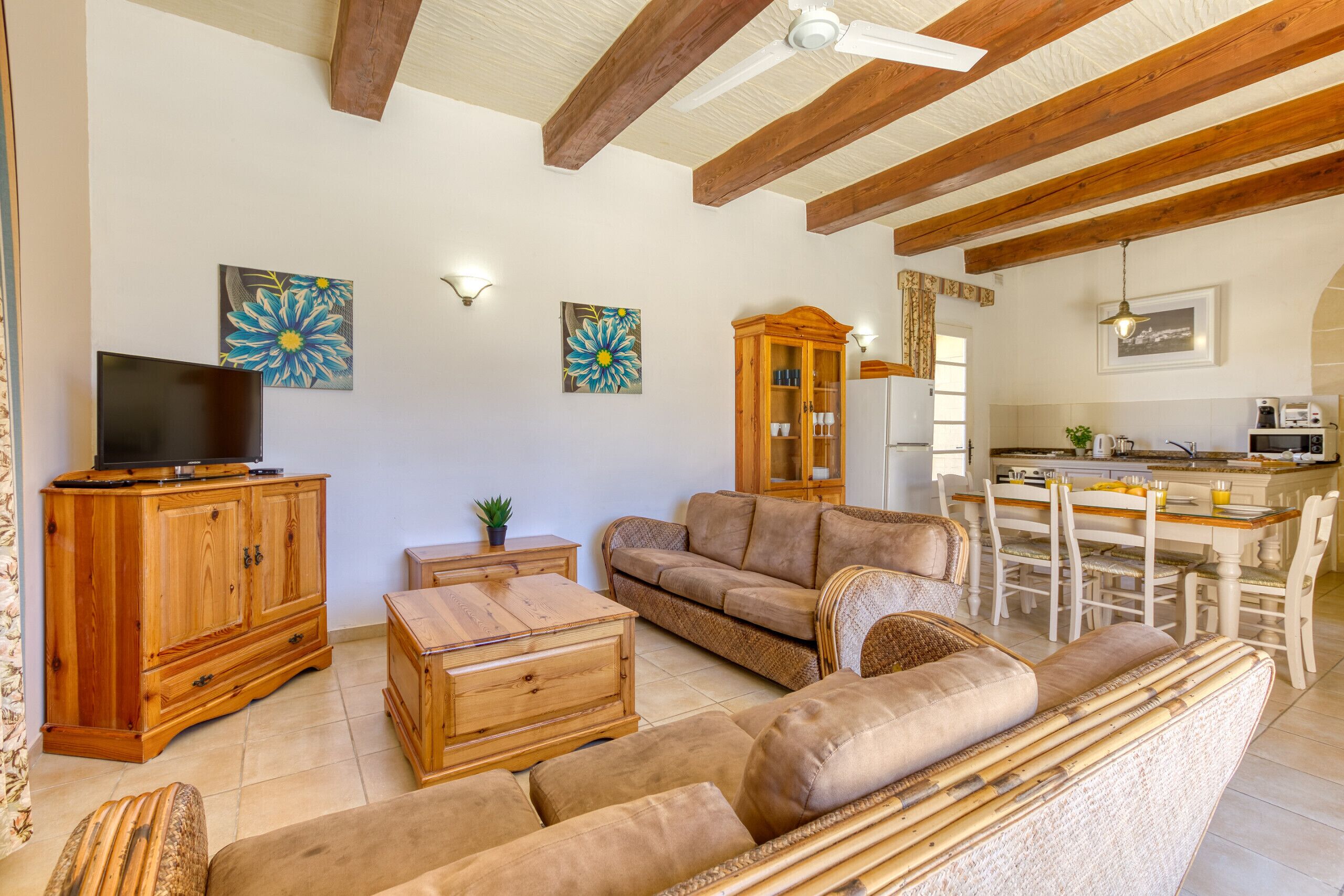 A living room with a sofa, wooden cabinet, and a television. There is a dining area with a table and chairs.