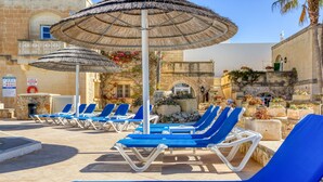 A pool area with blue lounge chairs and thatched umbrellas. - Villagg tal-Fanal - 2BDR (L-Ghasri)