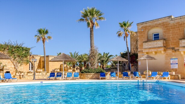 A swimming pool with blue chairs, palm trees, and a stone building with arched windows. - Villagg tal-Fanal - 2BDR (L-Ghasri)