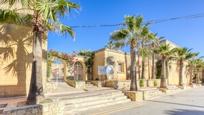 A hotel with a stone facade, palm trees, and a clear blue sky. - Villagg tal-Fanal - 2BDR (L-Ghasri)
