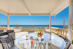 A round glass table with chairs, a glass of drink, and a flower vase on a balcony overlooking the sea. - 3387 Affaccio sul Mare by Barbarhouse (Castrignano del Capo)