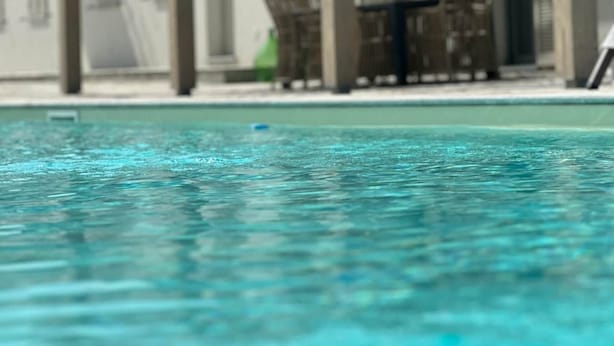 A swimming pool with clear water, surrounded by a building with multiple windows and covered outdoor seating areas. - Cascina Canelli - Apt. Alba, Cascina Canelli - Apt. Alba (Canelli)