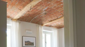 A bedroom with a wooden floor, a bed with white bedding, a brick ceiling, and a window with curtains. - Cascina Canelli - Apt. Alba, Cascina Canelli - Apt. Alba (Canelli)