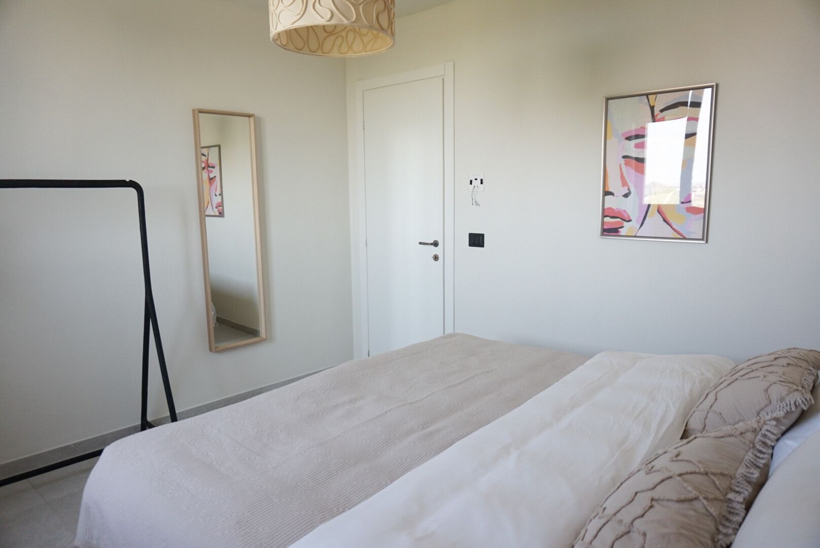 Quarto com cama, guarda-roupa, espelho e luminária na parede.