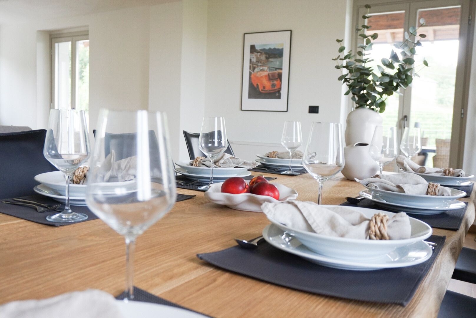 Une table à manger dressée pour un repas, avec plusieurs verres à vin, des assiettes et un saladier rempli de fruits.