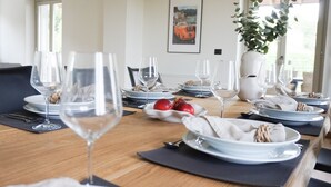 Uma mesa de jantar posta para refeição, com vários copos de vinho, pratos e uma tigela de frutas.