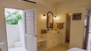 A bedroom with a bed, a bathroom with a sink and mirror, and a door leading to a balcony with plants. - Casablanca Oasis (Troncones)