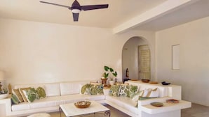 A spacious living room with a white sectional sofa, round ottomans, a ceiling fan, and a tiled floor. - Casablanca Oasis (Troncones)