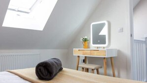 Ein Schlafzimmer mit Dachfenster, einem Bett mit zusammengelegtem Handtuch, einer weißen Kommode mit Spiegel und einer kleinen Pflanze.