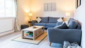 Ein stilvolles Wohnzimmer mit einem grauen Sofa, einem Couchtisch mit Büchern und einer Lampe.