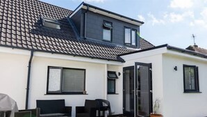 Ein modernes Haus mit einem Ziegeldach, einer überdachten Terrasse und Gartenmöbeln sowie einer Schiebetür.