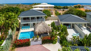 Ein Resort mit Swimmingpool, strohgedeckten Gebäuden und üppiger Vegetation.