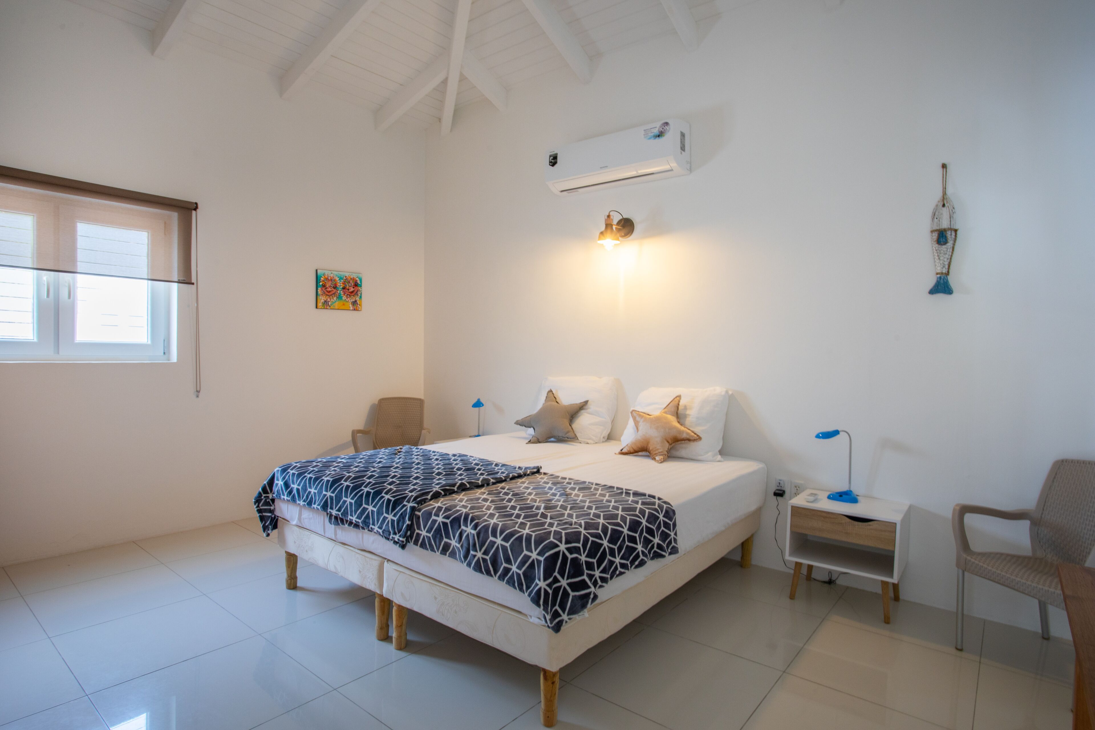Une chambre à coucher comprenant un lit, des tables de chevet, une chaise et un appareil de climatisation.