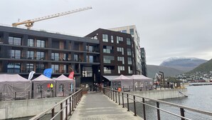 Un bâtiment moderne doté de nombreux balcons et de grandes fenêtres, une jetée avec une rambarde et une grue en arrière-plan.