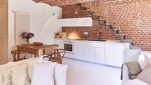 A compact kitchen with white cabinetry, a wooden dining table, and a brick wall. - AQVAE Unconventional Country House (Piemonte)