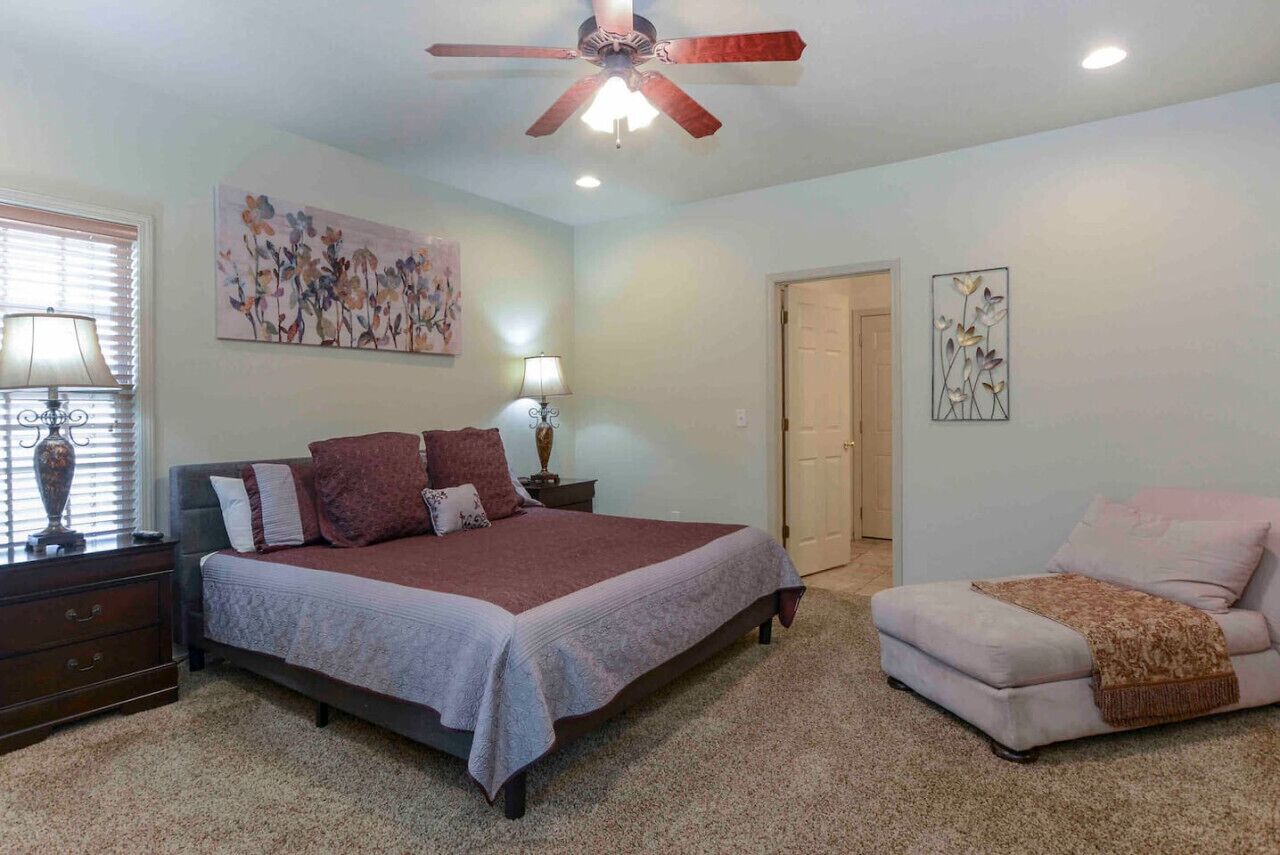 A bedroom with a bed, a chair, a ceiling fan, and artwork on the walls.