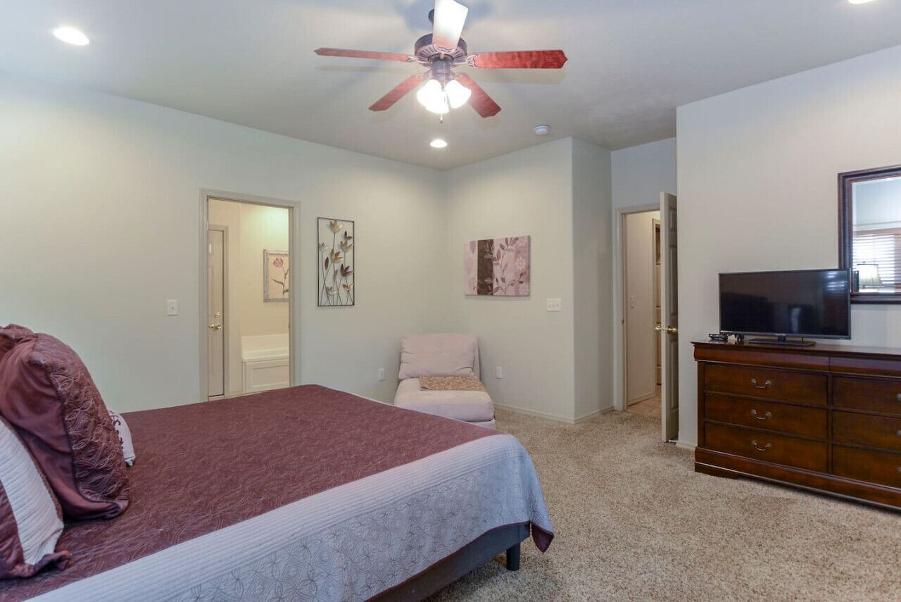 Une chambre à coucher avec un lit, une commode, un téléviseur et un ventilateur de plafond.