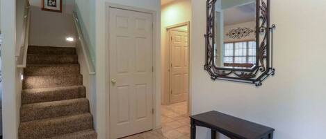 A hallway with a carpeted staircase, a white door, and a wall-mounted mirror.