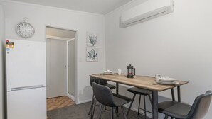 Une petite cuisine équipée avec un réfrigérateur blanc, une table à manger en bois avec quatre chaises et une cafetière.