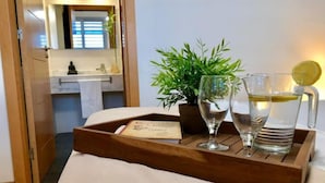 Un plateau en bois avec deux verres d’eau et une tranche de citron, une plante en pot et un menu, le tout posé sur une table dans une chambre d’hôtel.