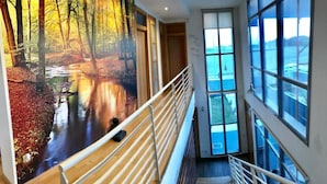 Un couloir orné d’une fresque représentant une scène de forêt, un escalier et de grandes fenêtres donnant sur l’extérieur.