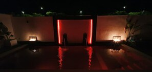 A nighttime pool area with red lighting and a central water feature. - Bali zen Moderno (Jarana)