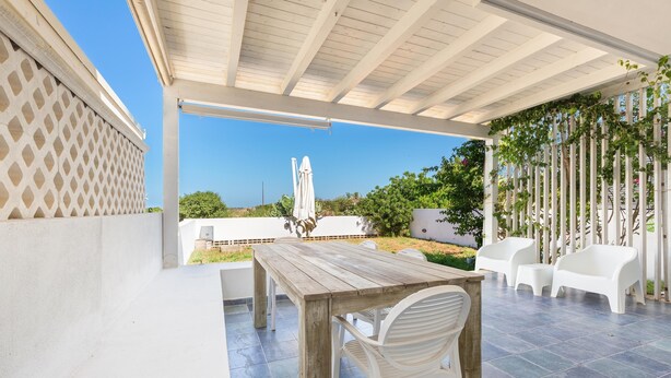 An outdoor patio with a wooden table and white chairs, a white umbrella, and a view of the sea. - 3590 Charà by Barbarhouse (Ugento)