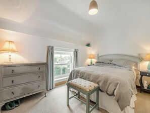 Un dormitorio con cama, mesitas de noche, cómoda, ventana con cortinas y una lámpara colgante.