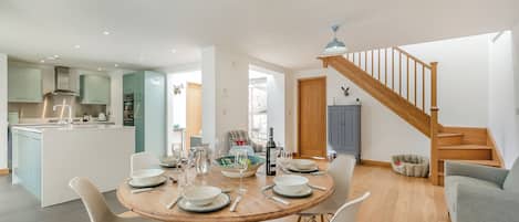 A modern kitchen with a central island, a dining area with a round table and chairs, and a staircase leading to an upper level.