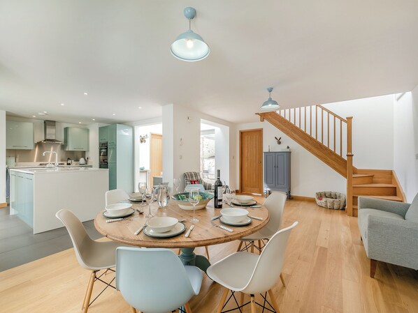 Una cocina moderna con una isla central, una zona de comedor con mesa redonda y sillas, y una escalera que sube a un nivel superior.
