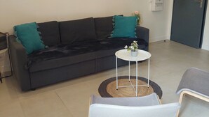Una sala de estar con un sofá gris oscuro, cojines color turquesa, una pequeña mesa blanca con una planta en maceta y un cuadro en la pared.