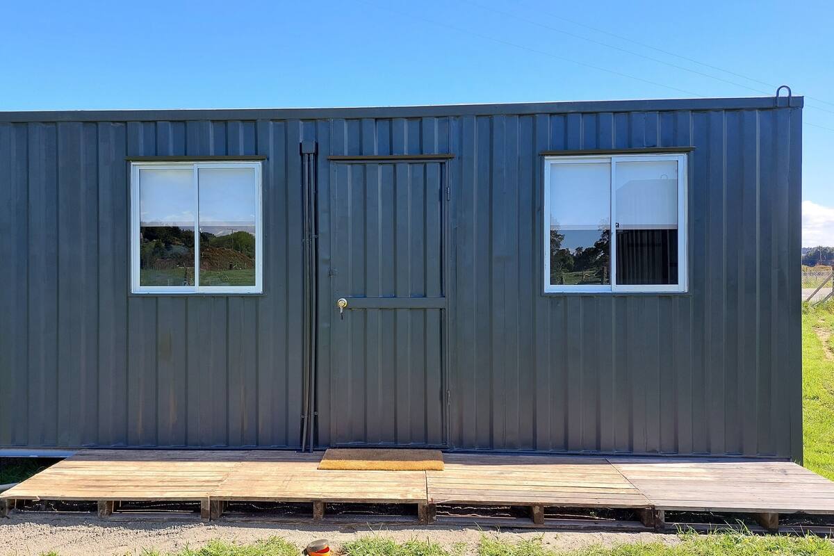 A small, single-story metal building with a dark gray exterior, two windows, and a door.