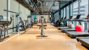 A gym with treadmills, exercise equipment, and large windows offering views of buildings. - Maison Privee - Sleek and Sunny Apt in Business Bay w/ Canal Views (Dubai)