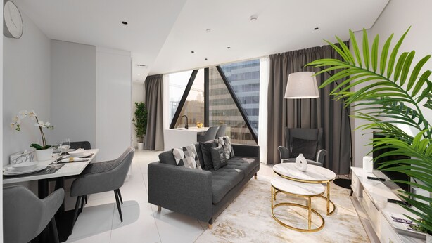A modern living room with a sofa, dining table, and chairs, a coffee table, and a large window with curtains. - Maison Privee - Sleek and Sunny Apt in Business Bay w/ Canal Views (Dubai)