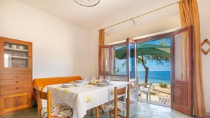 A dining area with a table set for two, a wooden cabinet, and a view of the beach through an open door. - 3533 Il Giglio Azzurro by Barbarhouse (Salve)