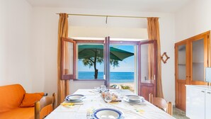 A dining area with a table set for two, a sofa, and a view of the sea through open windows. - 3533 Il Giglio Azzurro by Barbarhouse (Salve)