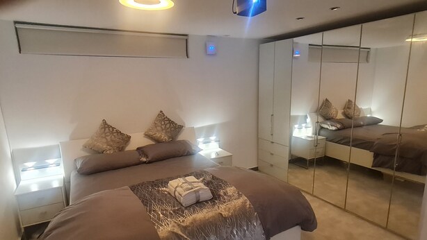 Een moderne slaapkamer met een groot bed, nachtkastjes, een spiegel en een kledingkast.